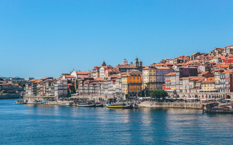 A wide shot of boats on the body of water near houses and buildings in Porto, Portugal